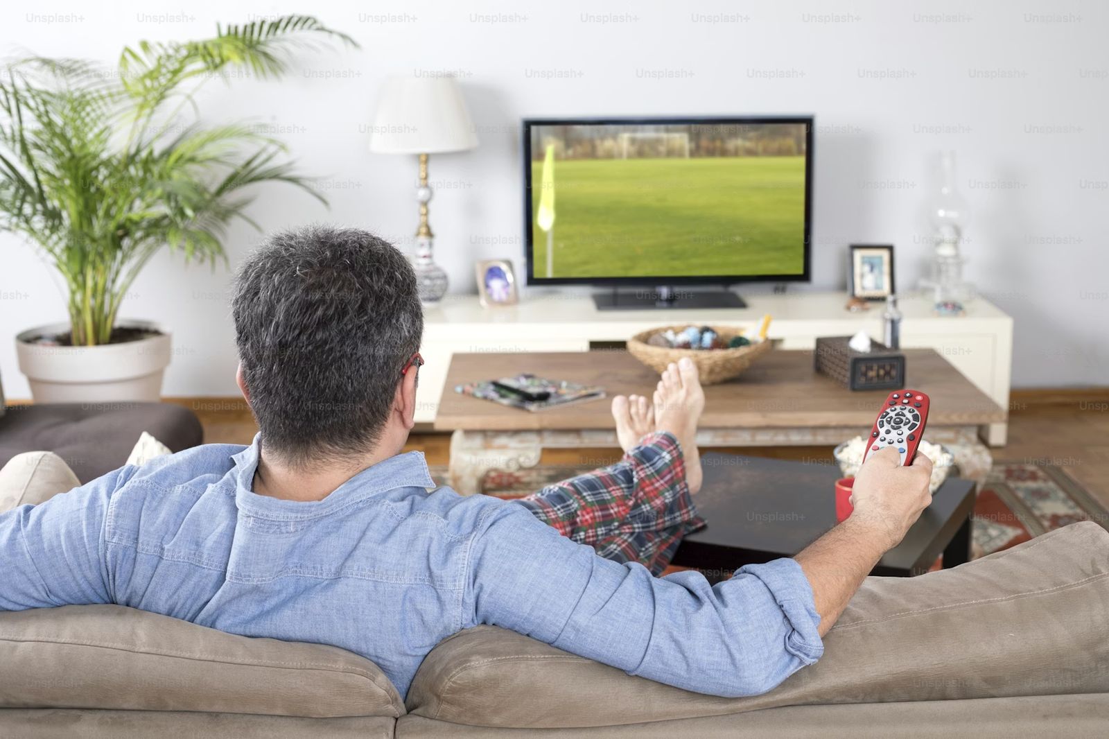 Hands holding a TV remote pointed at a flat-screen TV